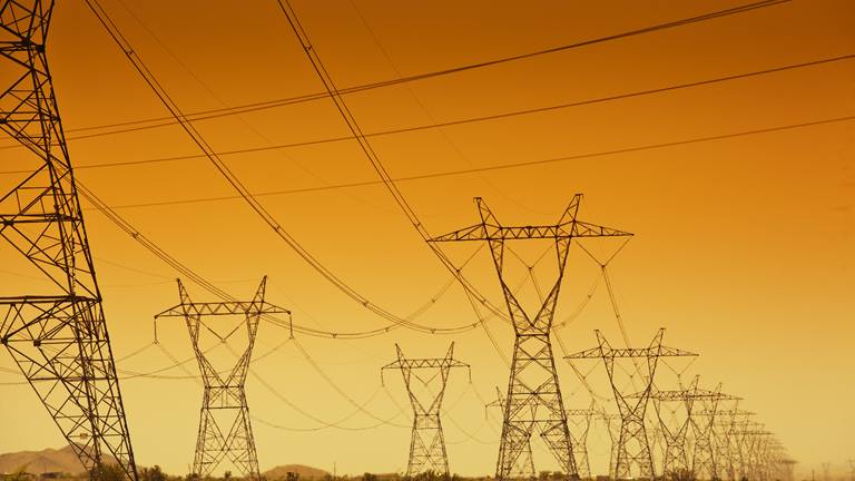 black transmission towers set against an orange and yellow sky